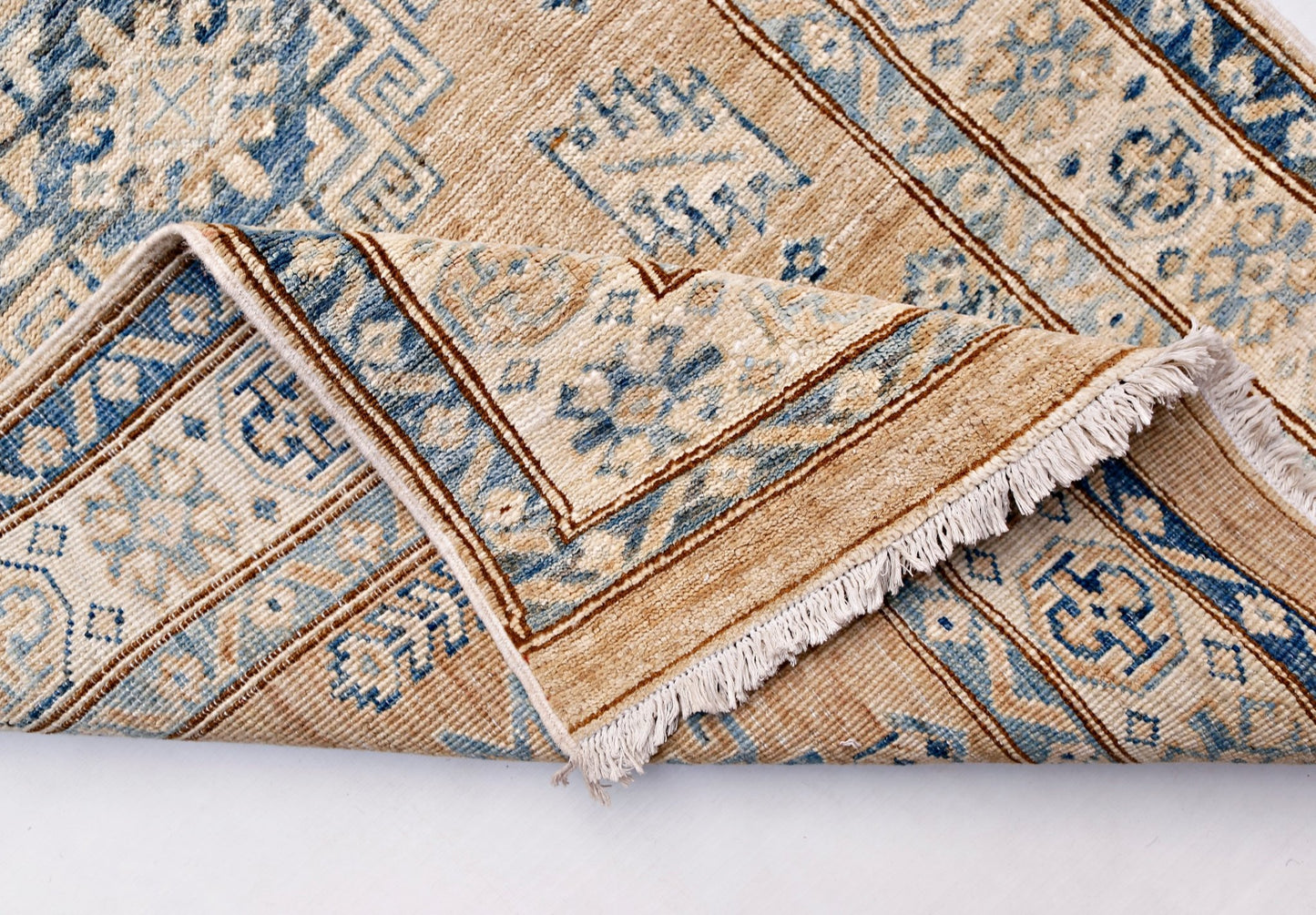 A handmade Afghan Super Kazakh runner rug featuring traditional blue motifs on a tan wool base.