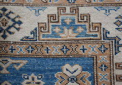 A close-up of a handmade Afghan Super Kazakh runner featuring traditional geometric motifs in blue and tan.