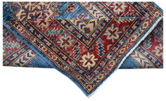 A folded Afghan Super Kazakh runner featuring traditional geometric motifs in red and blue wool.