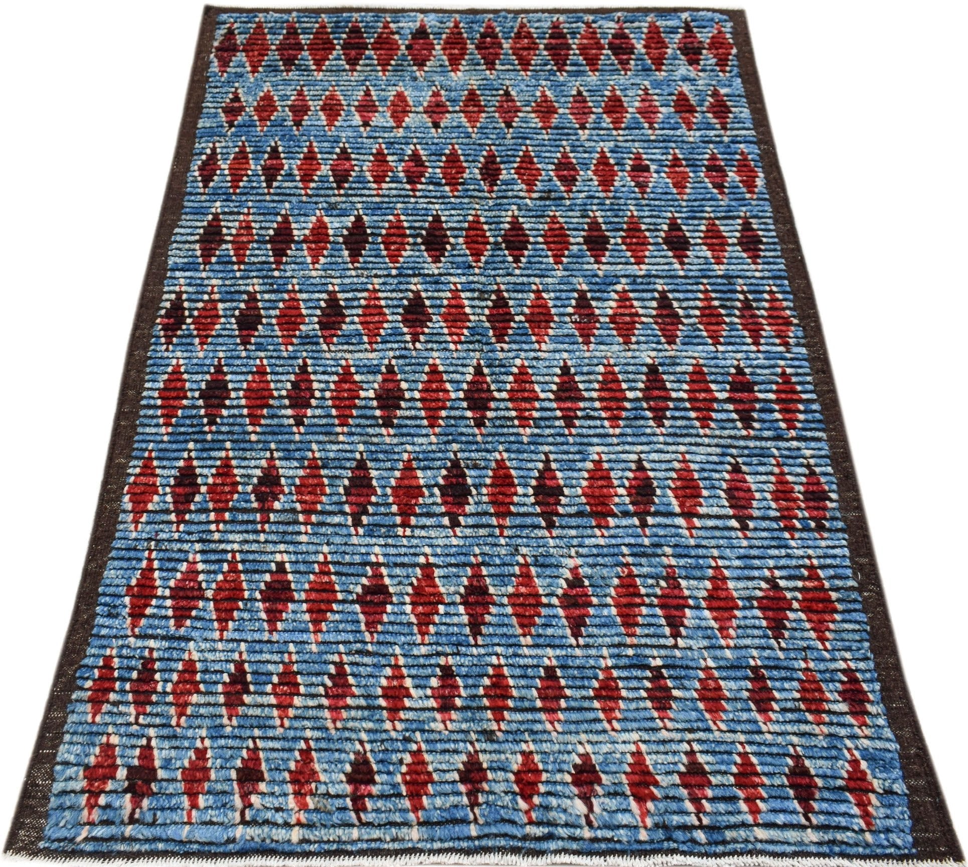 Hand-knotted Afghan rug featuring a blue background with a repeating red geometric diamond pattern.