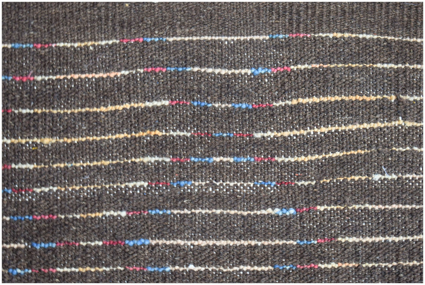 A dark brown hand-knotted wool rug featuring horizontal stripes with small colorful accents.