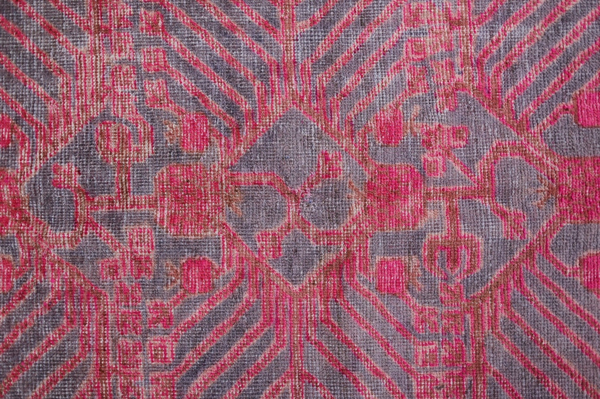 An antique handwoven Khotan rug featuring an intricate pomegranate pattern in vibrant pink.