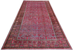An antique handwoven Khotan rug featuring a vibrant pink pomegranate pattern on a grey background.