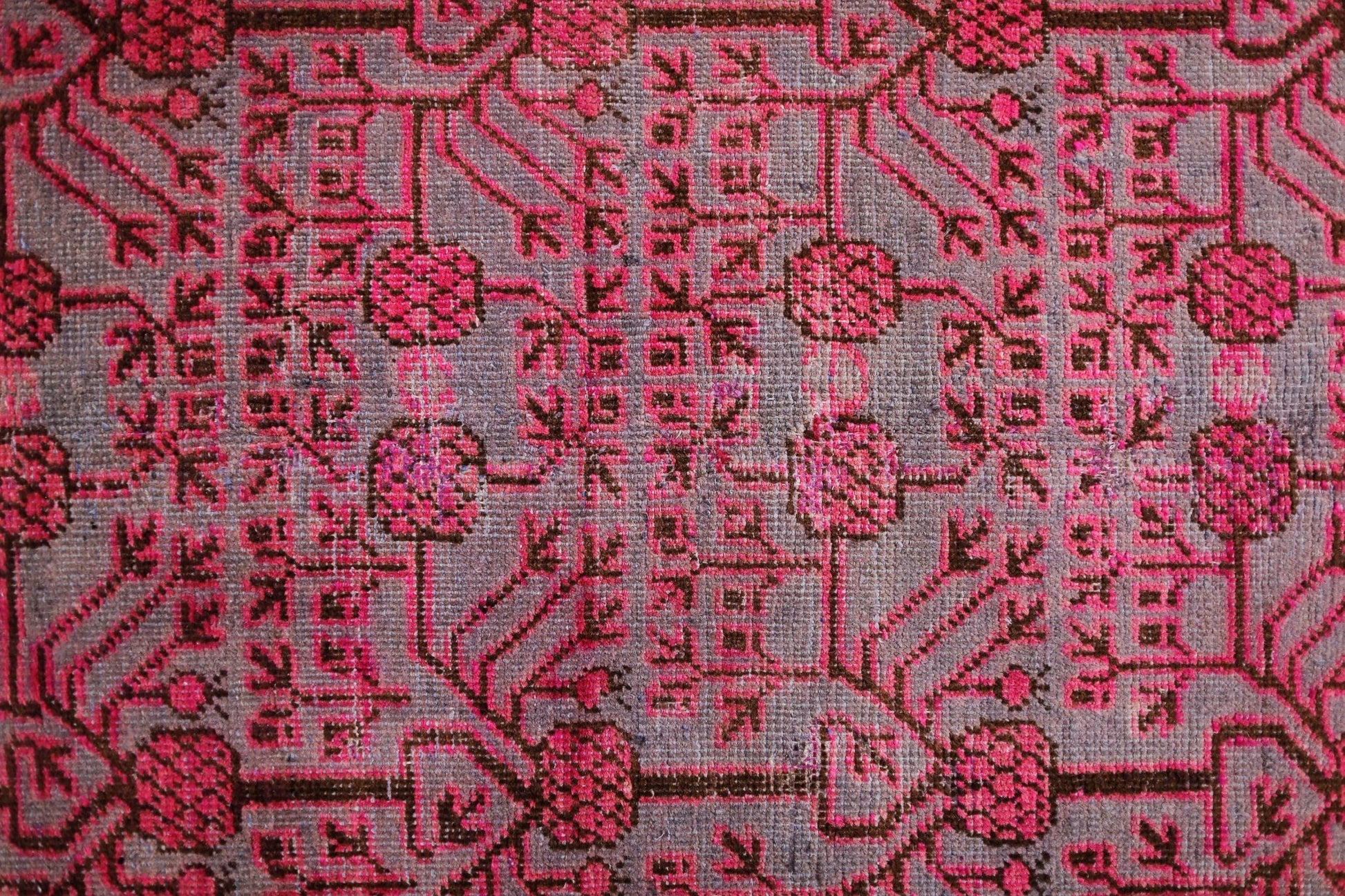 An antique handwoven Khotan rug featuring an intricate pomegranate pattern in vibrant pink.