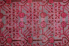 An antique handwoven Khotan rug featuring an intricate pomegranate pattern in vibrant pink.