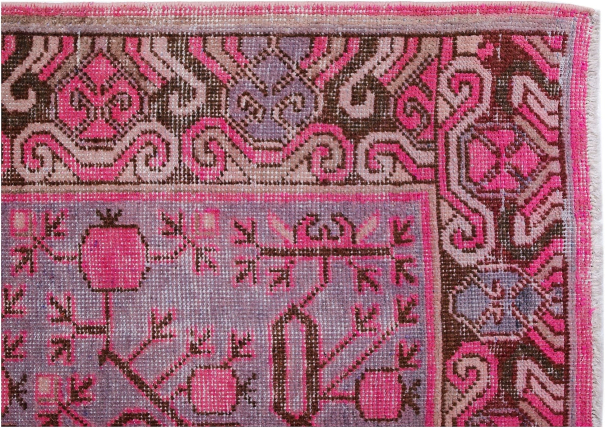 An antique handwoven Khotan rug featuring a vibrant pink pomegranate pattern on a purple field.