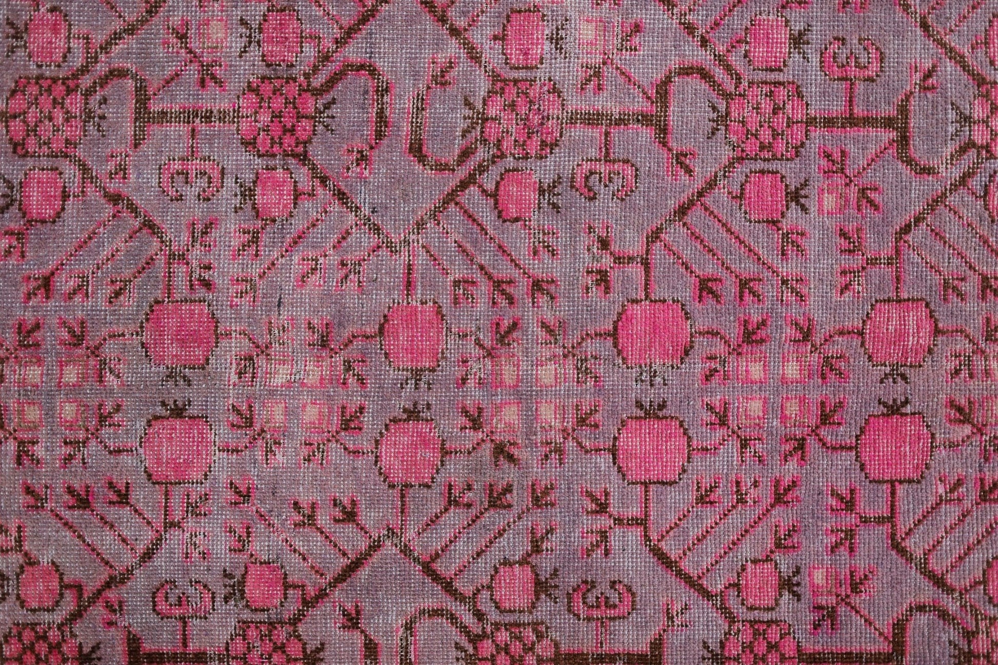 An antique handwoven Khotan rug featuring an intricate pomegranate pattern in vibrant pink.