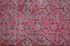 An antique handwoven Khotan rug featuring an intricate pomegranate pattern in vibrant pink.
