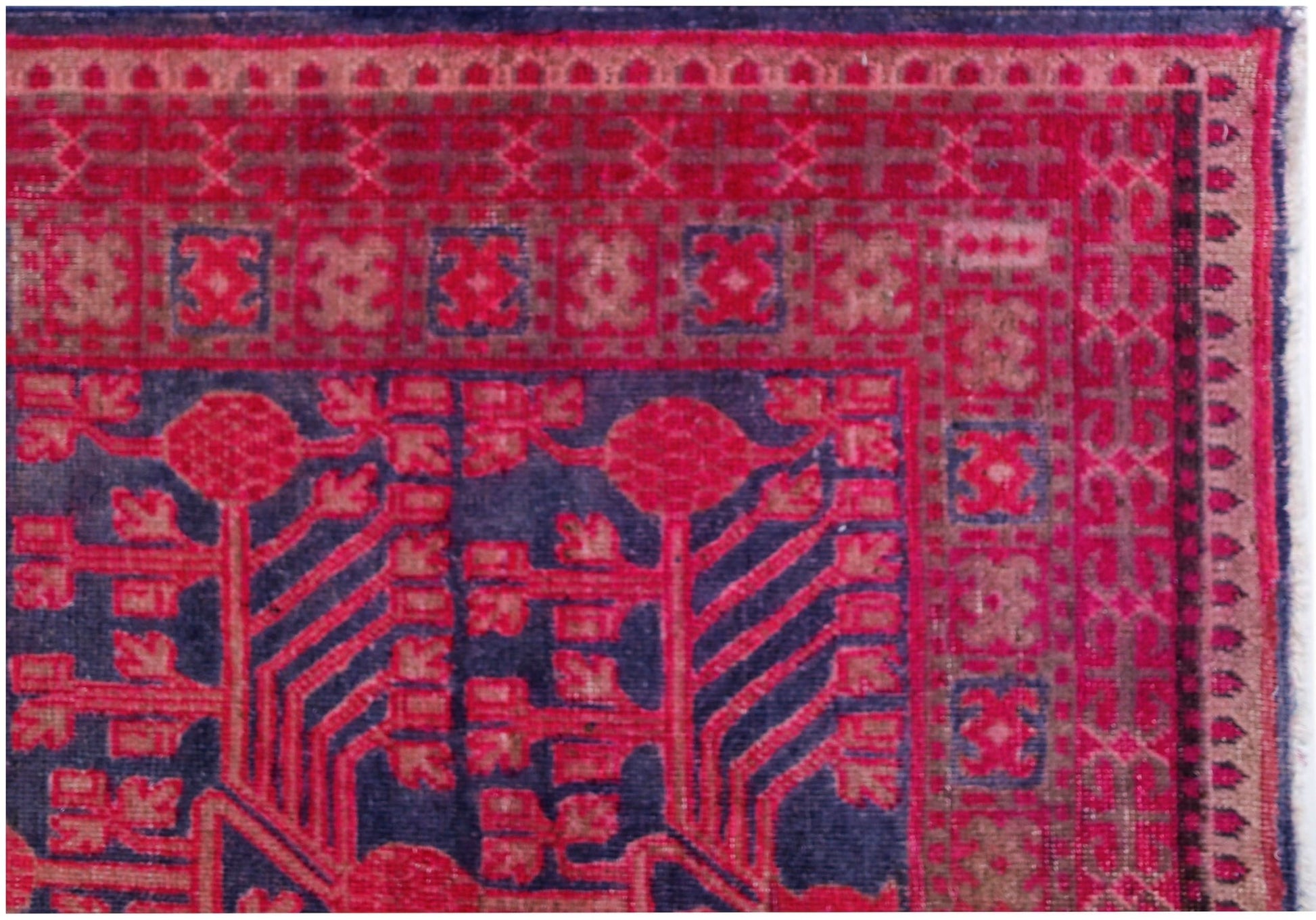 An antique handwoven Khotan rug featuring a vibrant pink pomegranate pattern on a dark blue field.