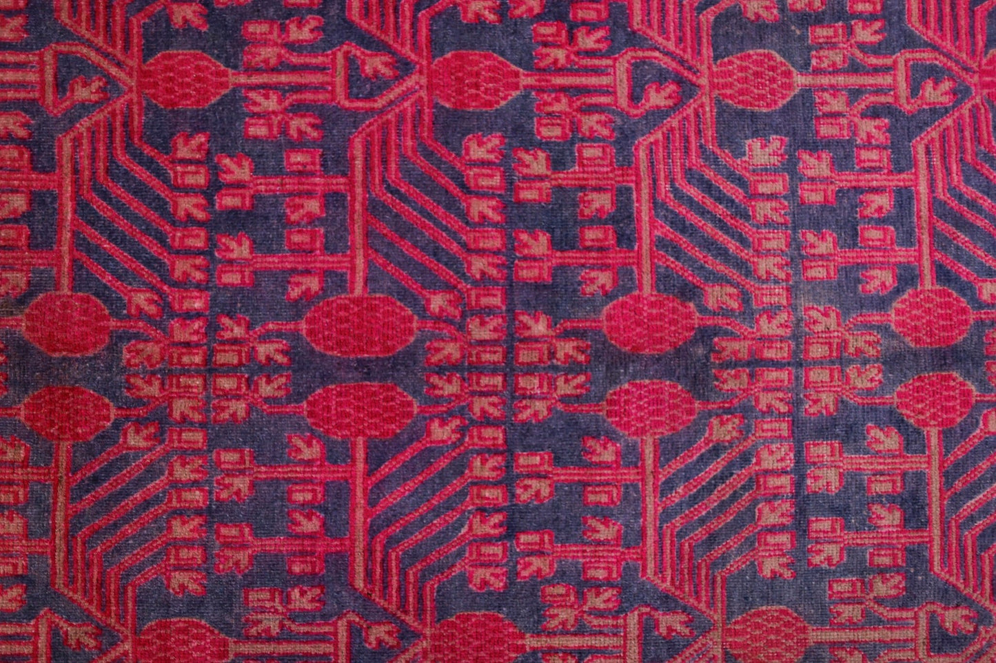 An antique handwoven Khotan rug featuring an intricate pink pomegranate pattern on a dark field.