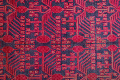 An antique handwoven Khotan rug featuring an intricate pink pomegranate pattern on a dark field.