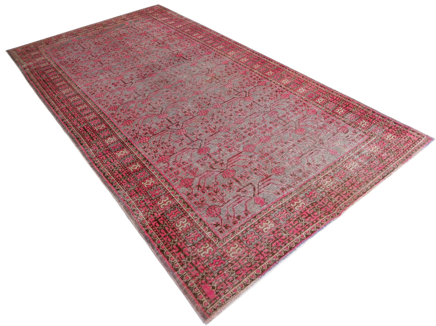 An antique handwoven Khotan rug featuring a vibrant pink pomegranate pattern on a grey field.