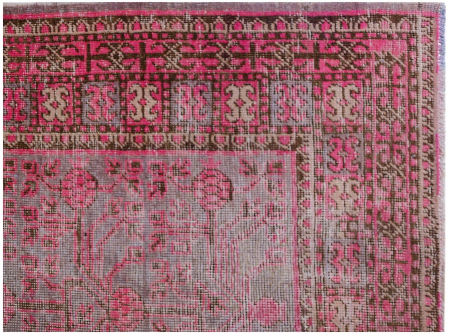 An antique handwoven Khotan rug featuring a vibrant pink pomegranate pattern on a grey background.