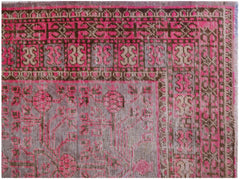 An antique handwoven Khotan rug featuring a vibrant pink pomegranate pattern on a grey background.