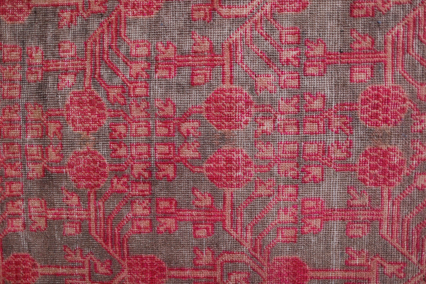 An antique handwoven Khotan rug featuring an intricate pomegranate pattern in vibrant pink.