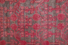 An antique handwoven Khotan rug featuring an intricate pomegranate pattern in vibrant pink.