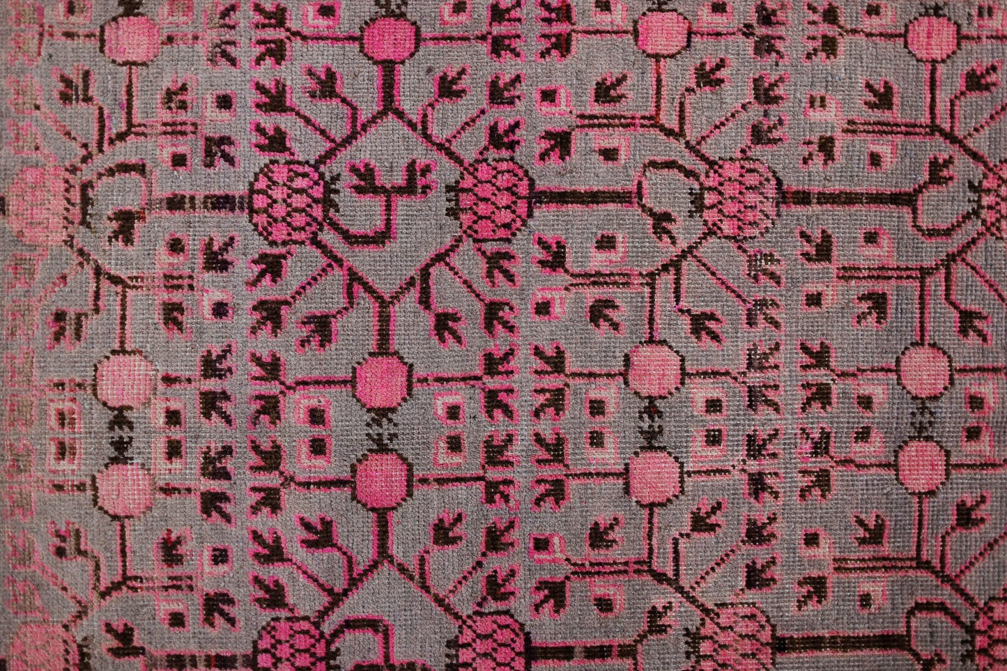 An antique handwoven Khotan rug featuring an intricate pink pomegranate pattern on a grey field.