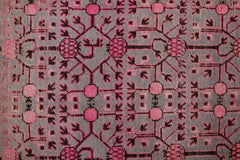 An antique handwoven Khotan rug featuring an intricate pink pomegranate pattern on a grey field.