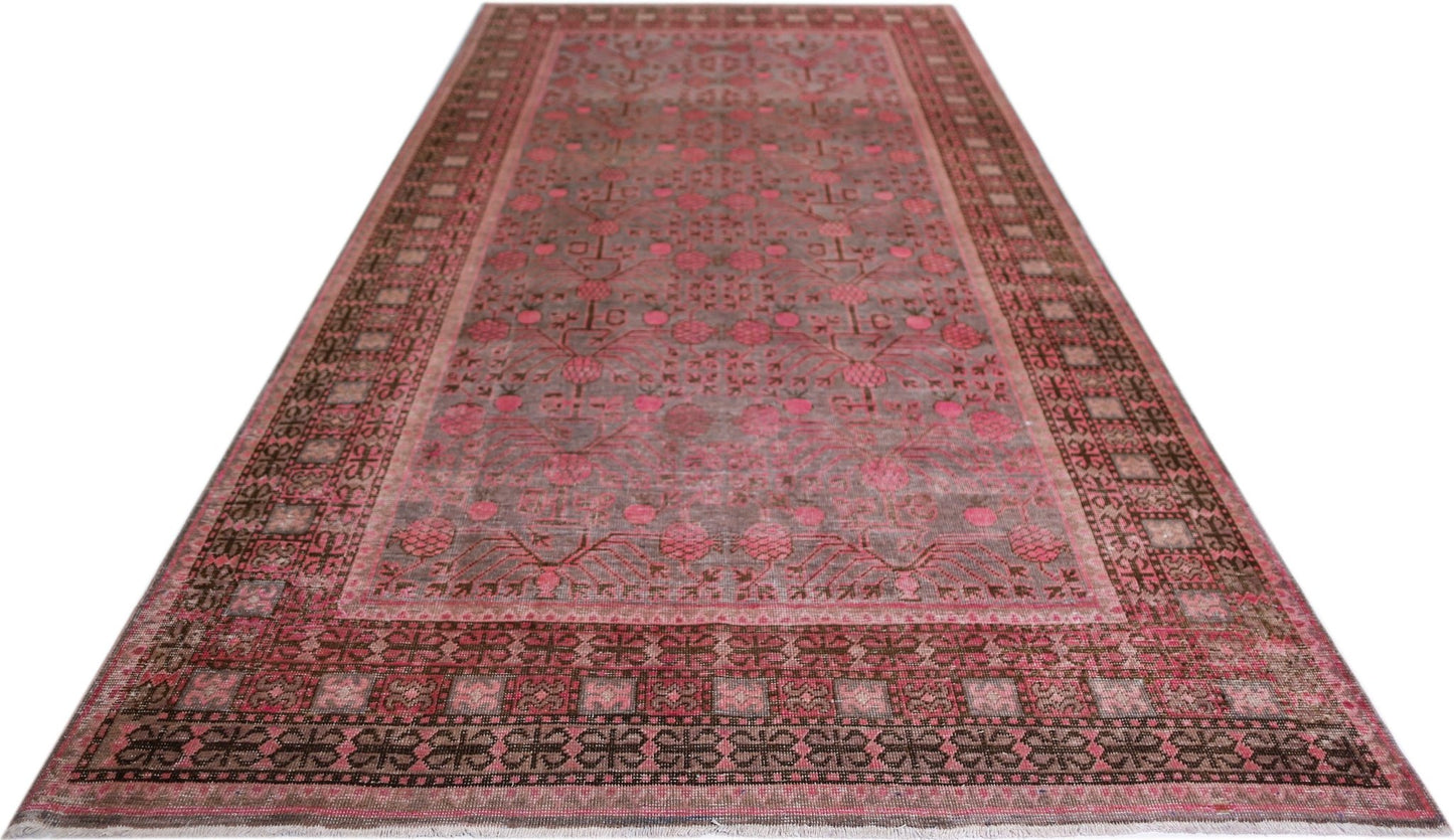 An antique handwoven Khotan rug featuring a pink pomegranate pattern on a muted background.
