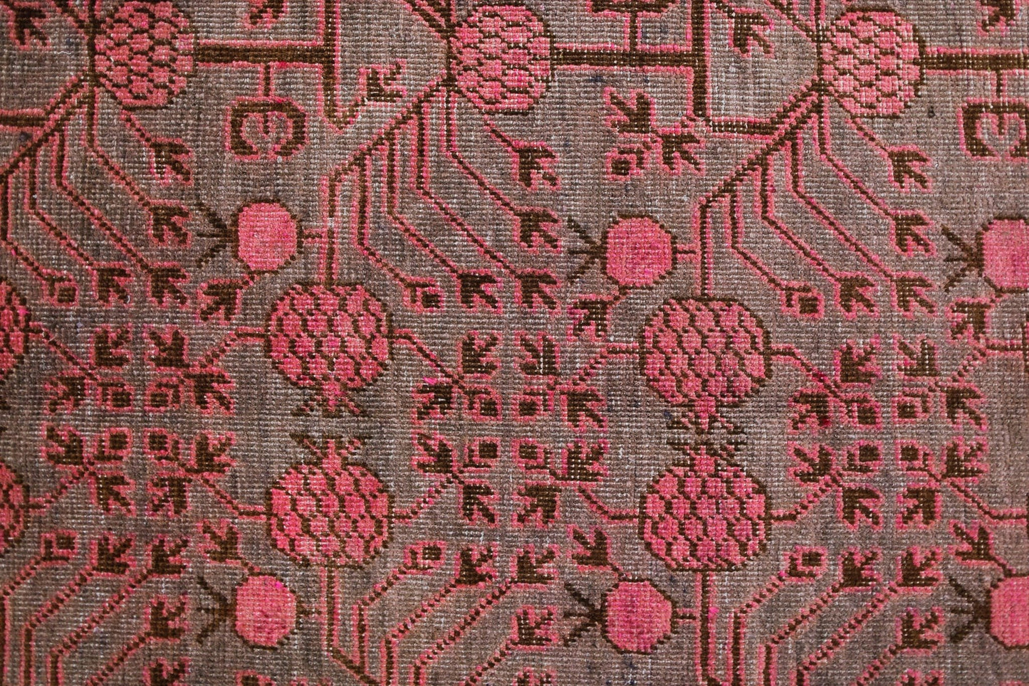 An antique handwoven Khotan rug featuring an intricate pink pomegranate pattern on a brown field.