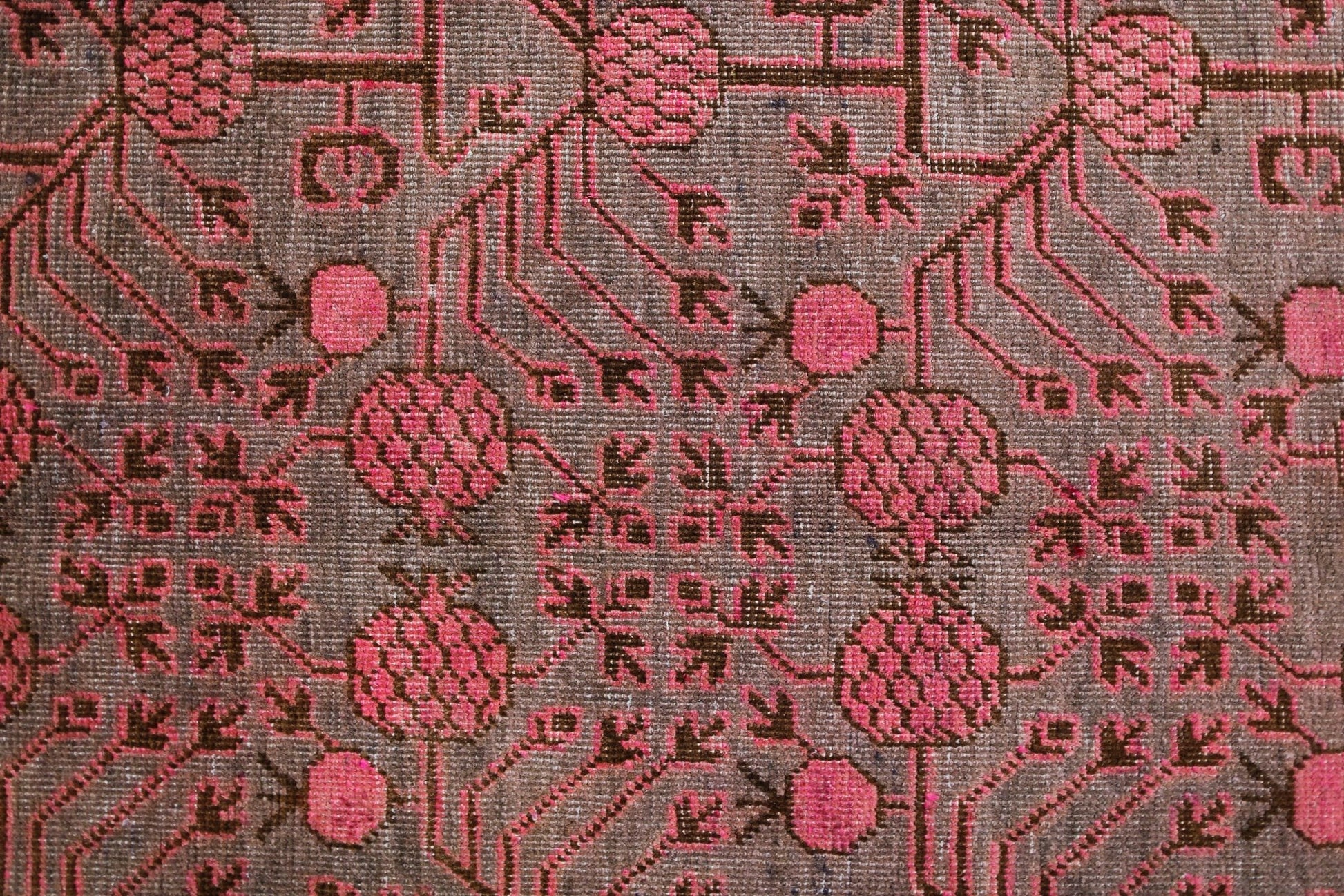 An antique handwoven Khotan rug featuring an intricate pink pomegranate pattern on a brown field.