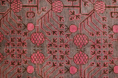 An antique handwoven Khotan rug featuring an intricate pink pomegranate pattern on a brown field.