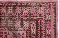 An antique handwoven Khotan rug featuring a geometric pomegranate pattern in pink and brown.