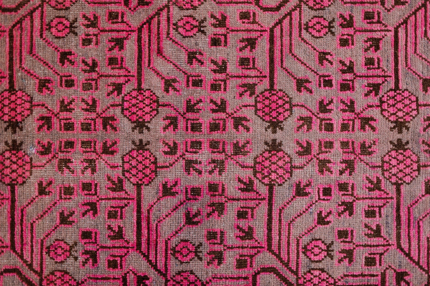 An antique handwoven Khotan rug featuring an intricate pink pomegranate pattern on a brown field.
