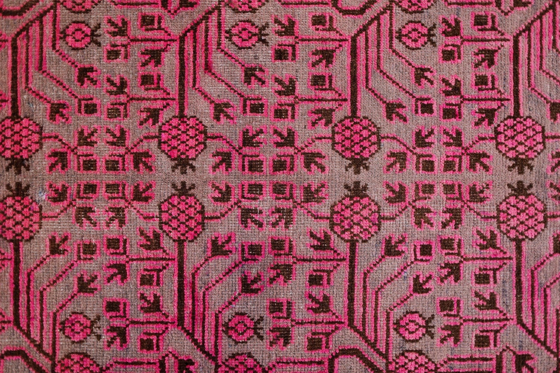 An antique handwoven Khotan rug featuring an intricate pink pomegranate pattern on a brown field.
