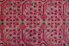 An antique handwoven Khotan rug featuring an intricate pink pomegranate pattern on a brown field.