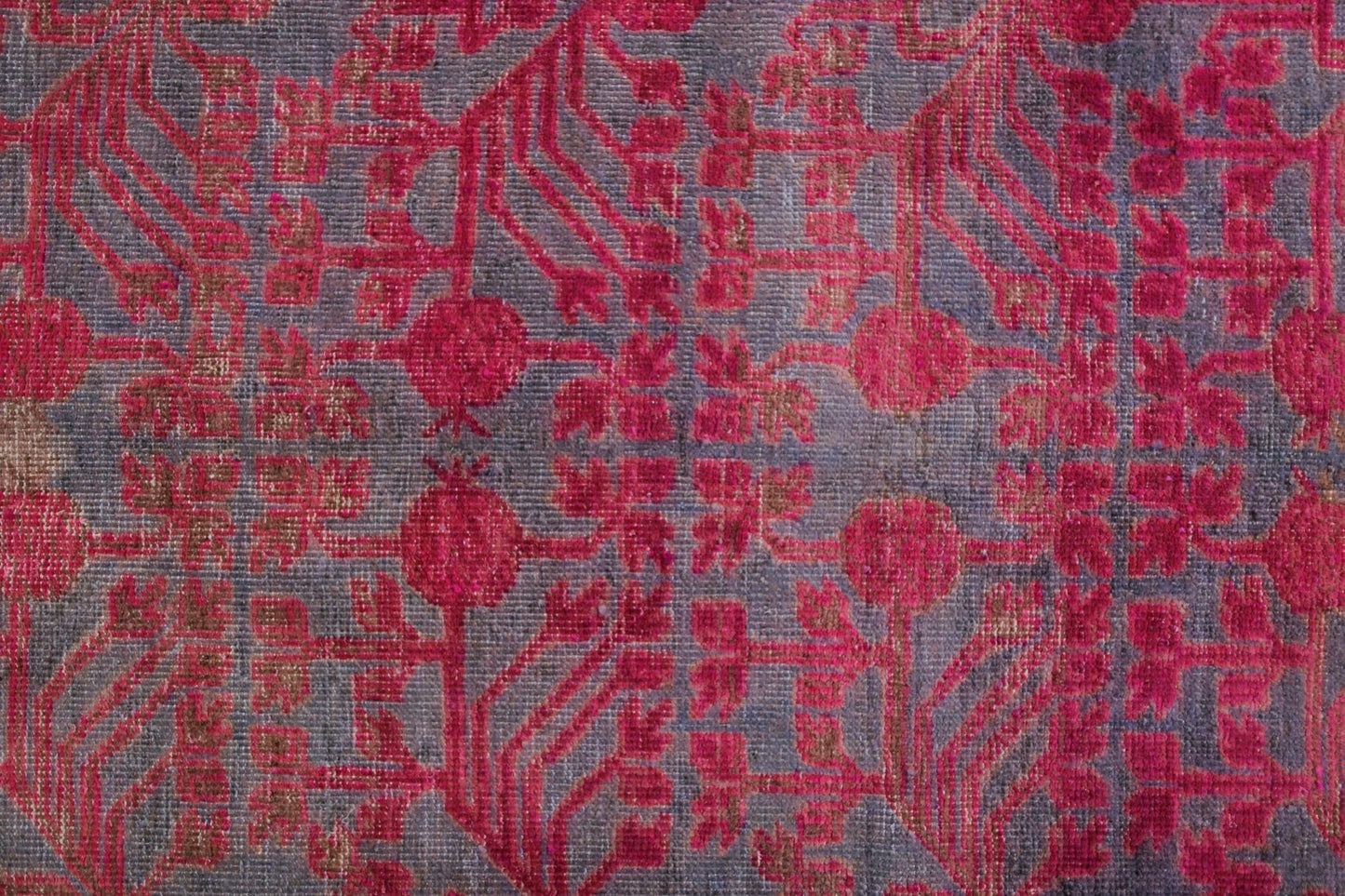 An antique handwoven Khotan rug featuring an intricate pink pomegranate pattern on a grey base.