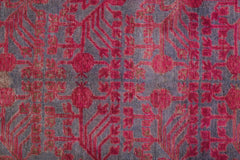 An antique handwoven Khotan rug featuring an intricate pink pomegranate pattern on a grey base.