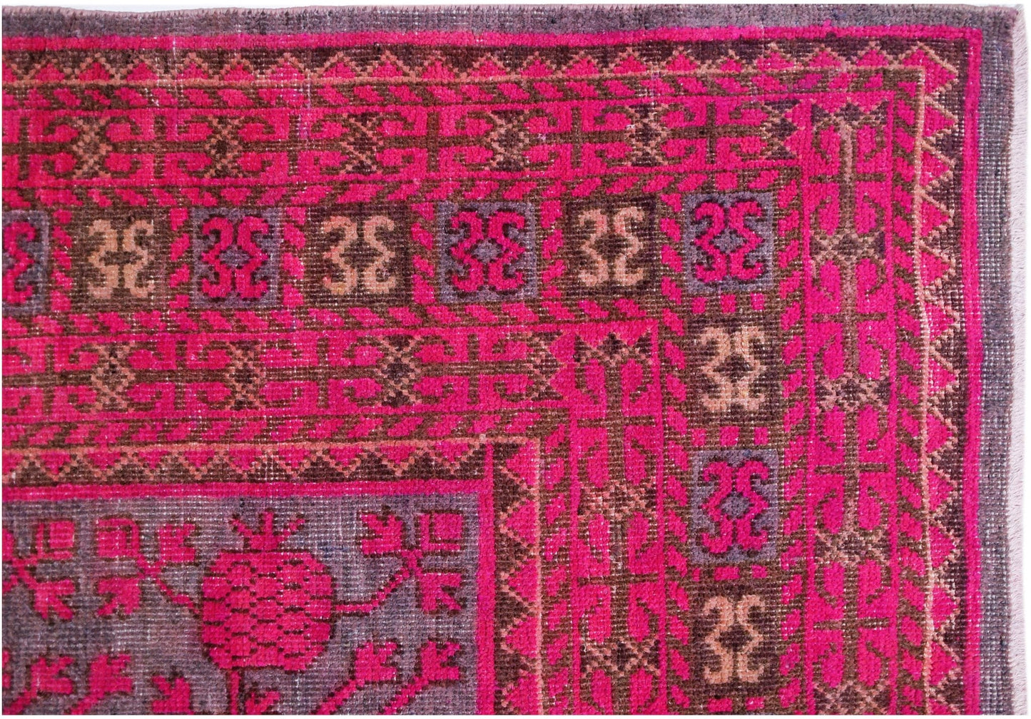 An antique handwoven Khotan rug featuring a vibrant pink pomegranate pattern on a wool base.