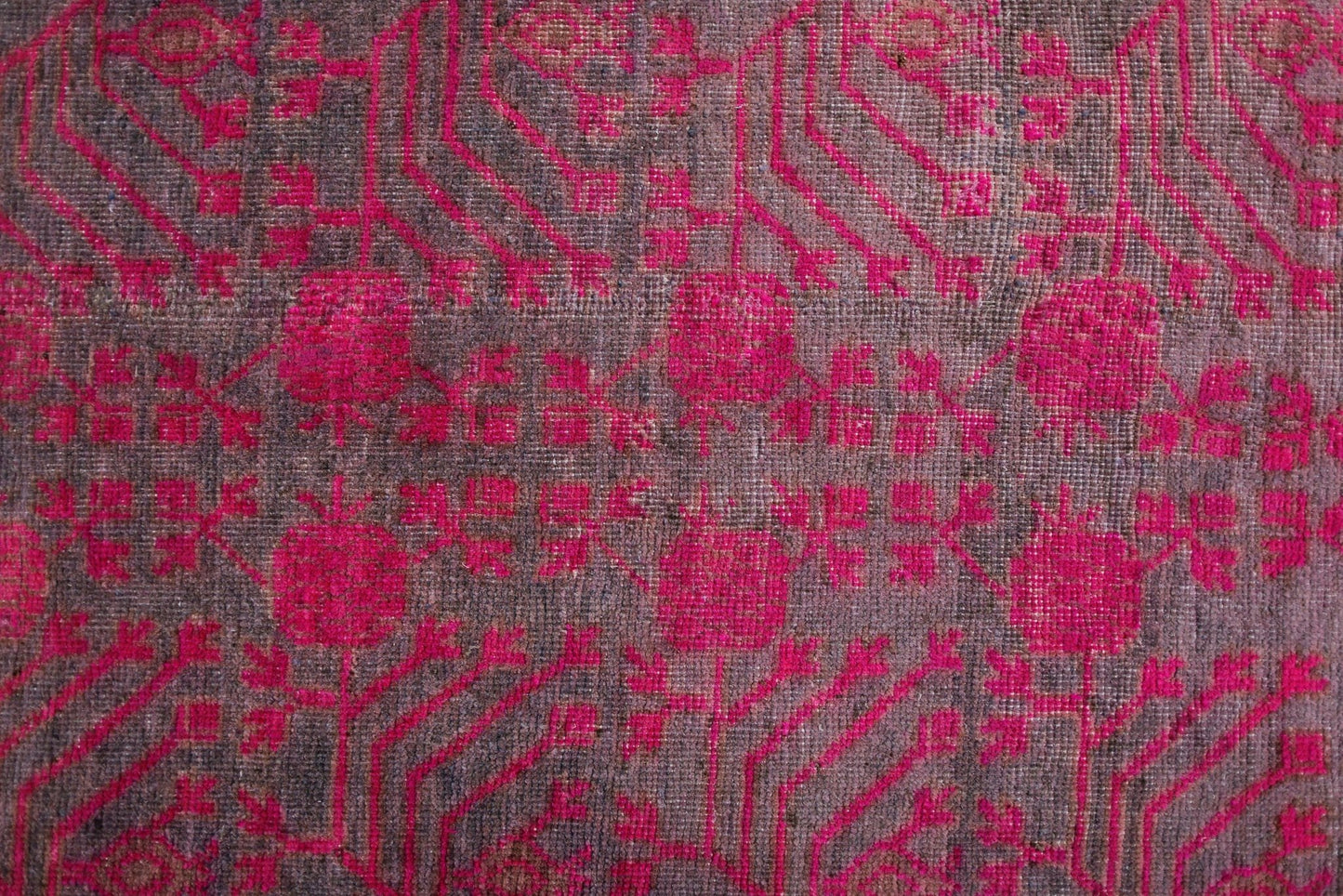 An antique handwoven Khotan rug featuring an intricate pomegranate pattern in vibrant pink.