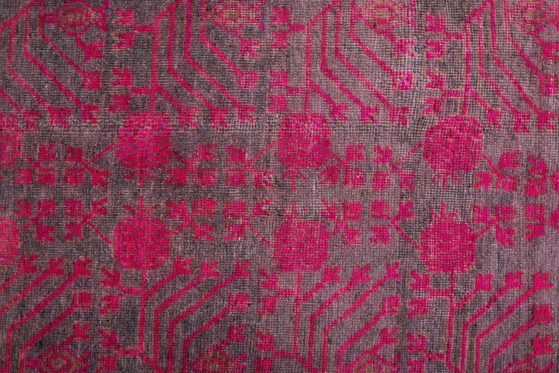An antique handwoven Khotan rug featuring an intricate pomegranate pattern in vibrant pink.