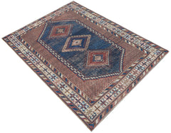 An antique handwoven Persian rug featuring a blue central field with geometric diamond motifs.