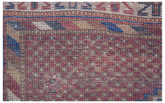 A close-up view of a handwoven antique Persian rug featuring a faded red and blue geometric pattern.