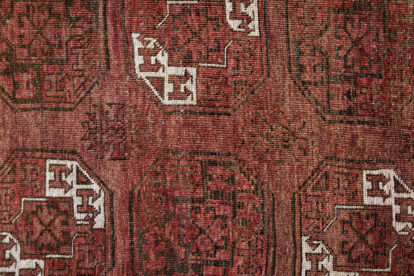 An antique Afghan Turkmen rug featuring traditional red wool and geometric elephant foot motifs.