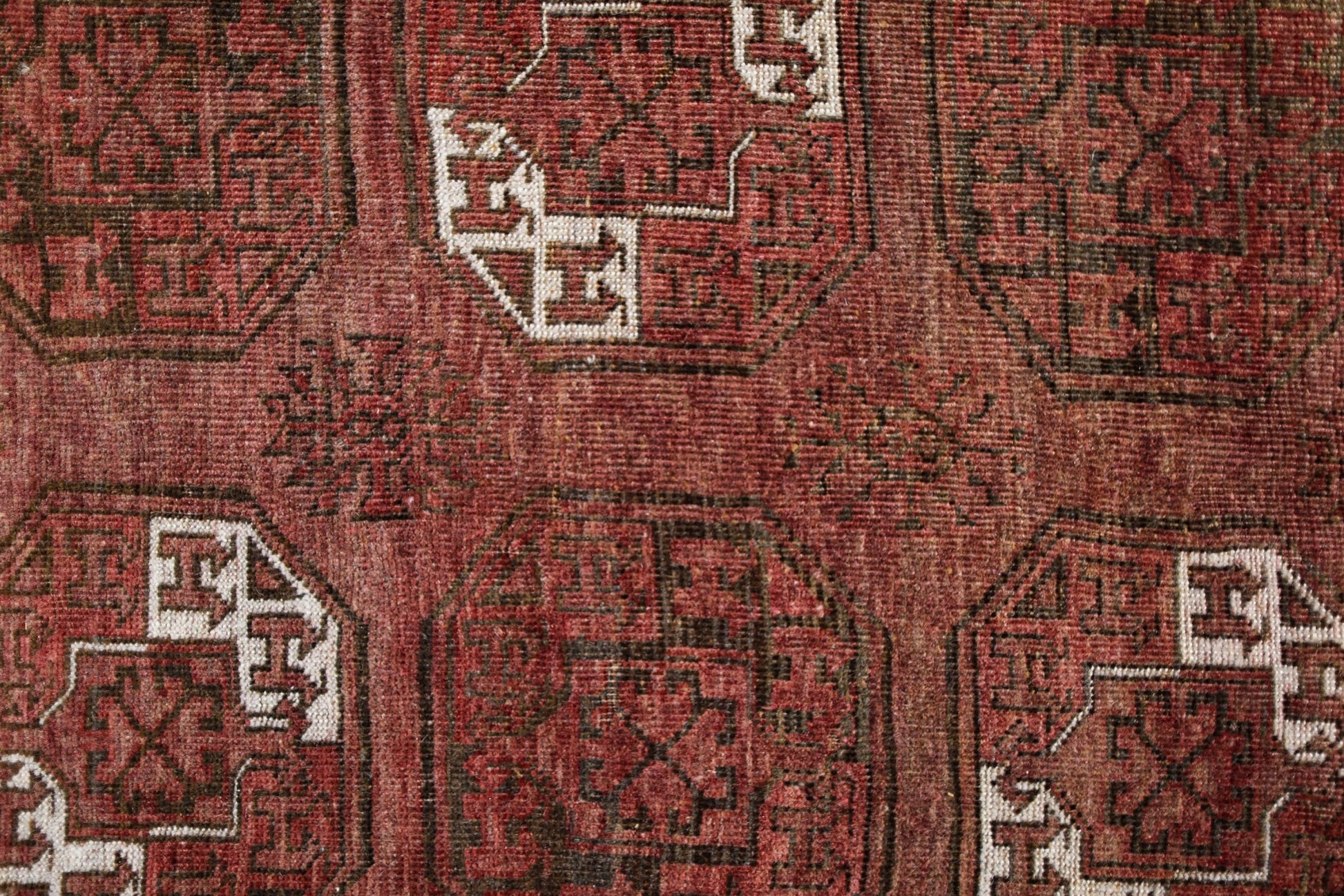 An antique Afghan Turkmen rug featuring traditional red wool and geometric elephant foot motifs.