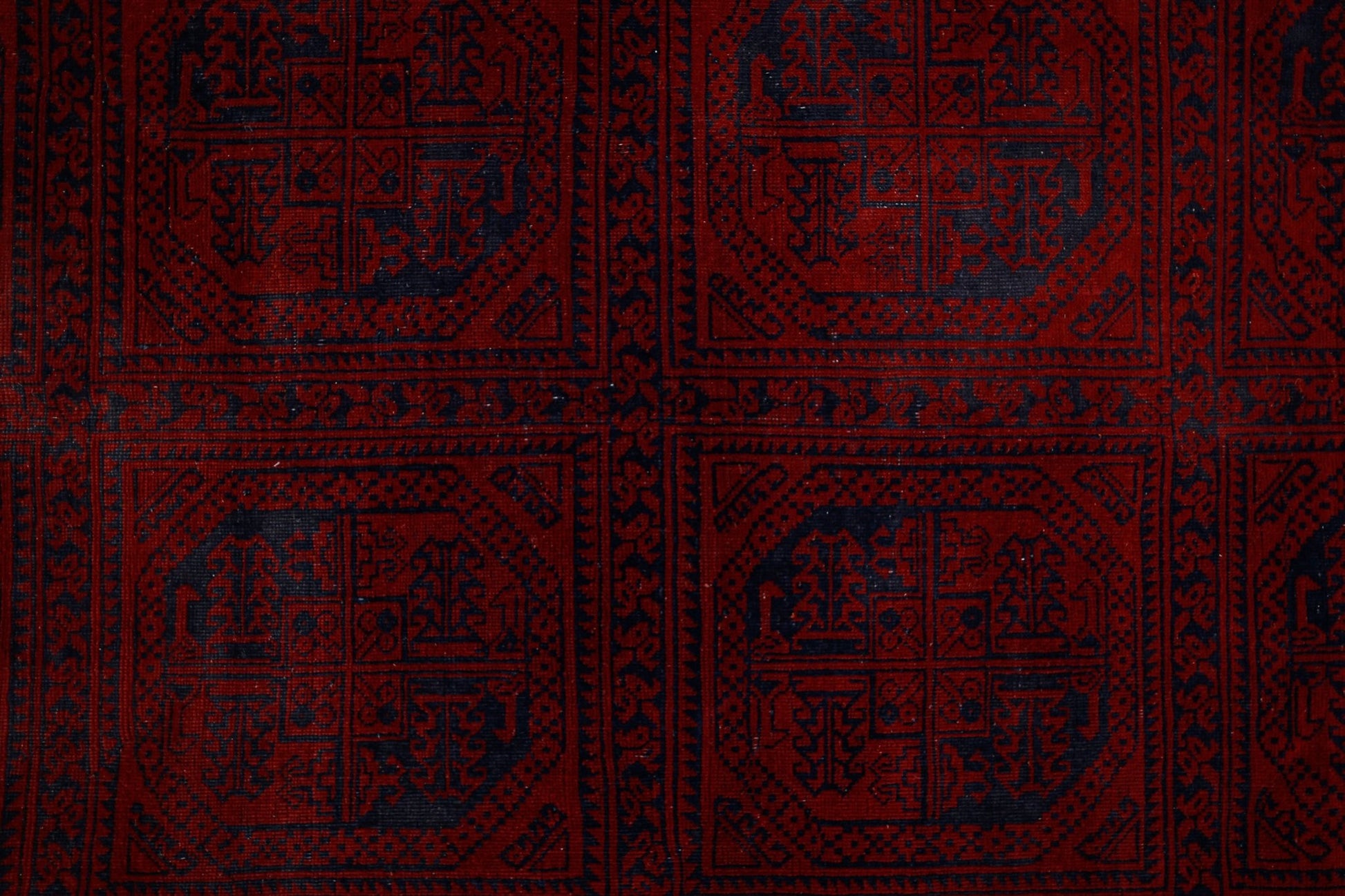 An antique Afghan Turkmen rug featuring a repeating pattern of dark blue elephant foot motifs on a deep red background.