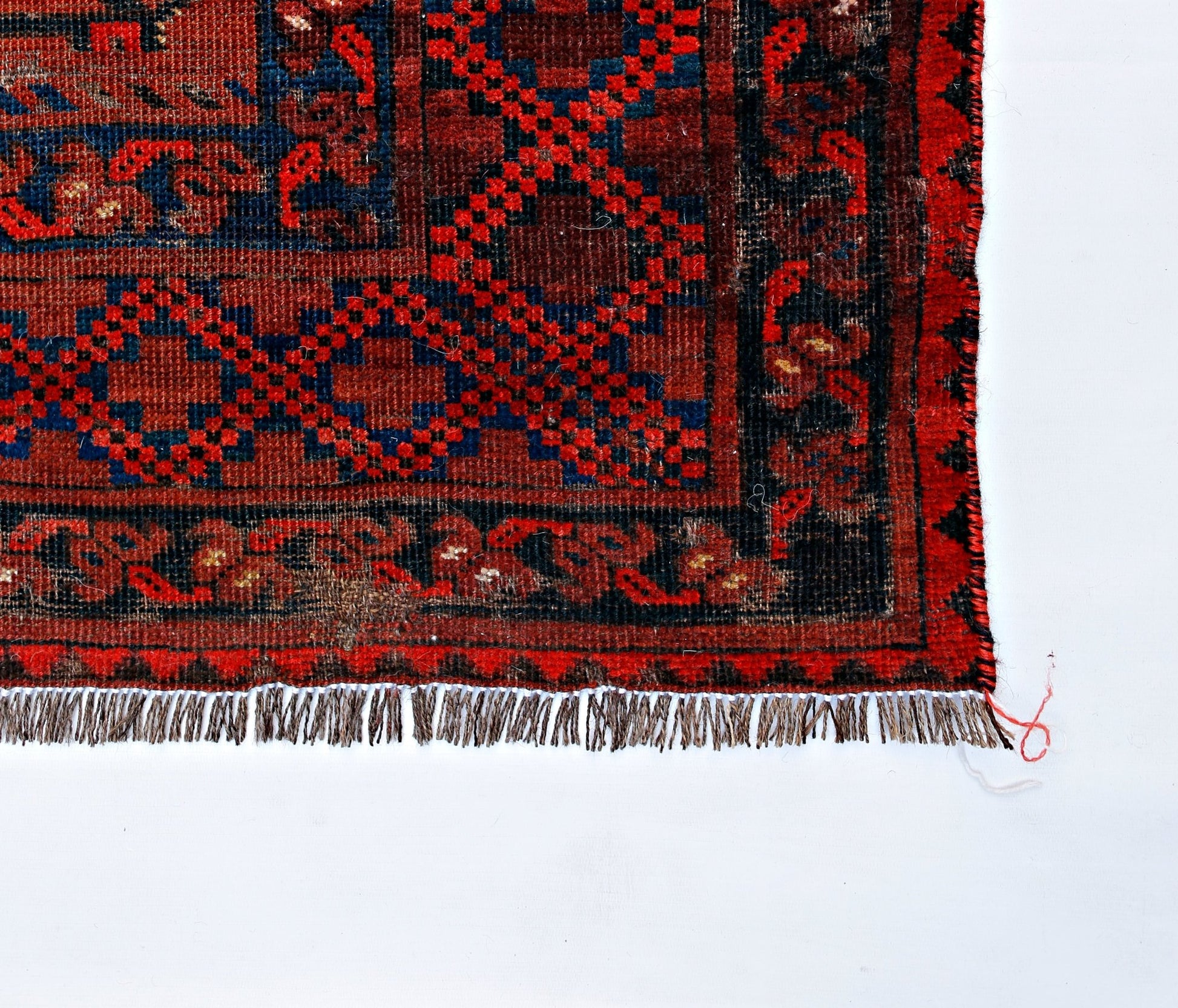 An antique Afghan Turkmen rug featuring a geometric red and blue pattern with a fringed edge.