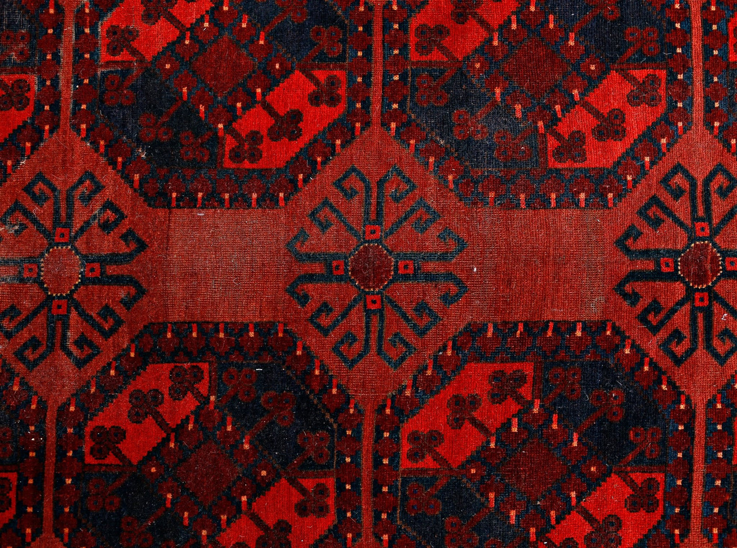 An antique Afghan Turkmen rug featuring a repeating geometric pattern in deep red and black.