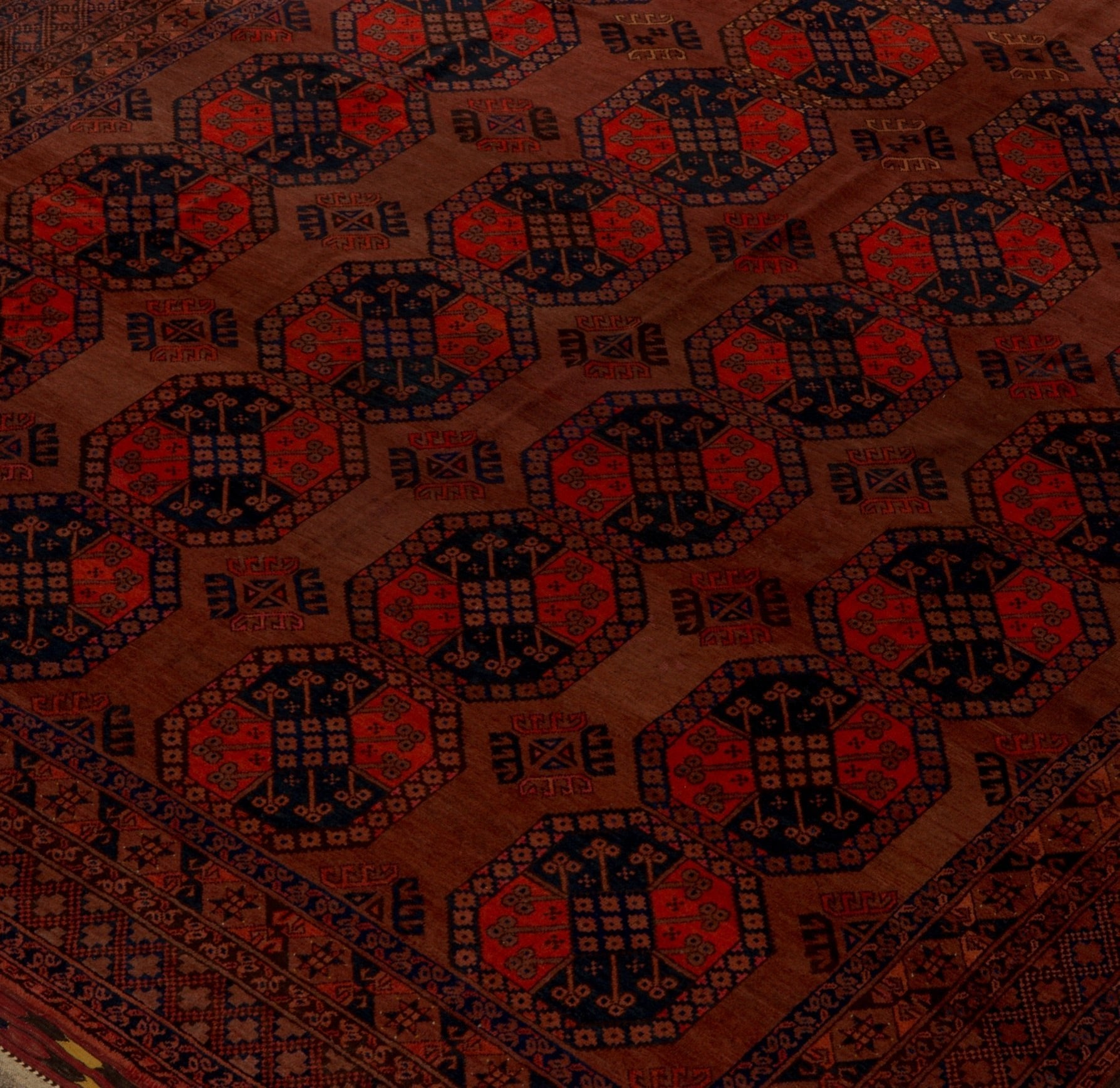 An antique Afghan Turkmen rug featuring a repeating geometric gul pattern in red and dark blue.