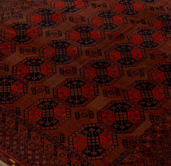 An antique Afghan Turkmen rug featuring a repeating geometric gul pattern in red and dark blue.