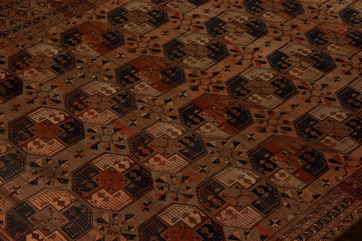 An antique Afghan Turkmen rug featuring a repeating geometric pattern in earthy tones.