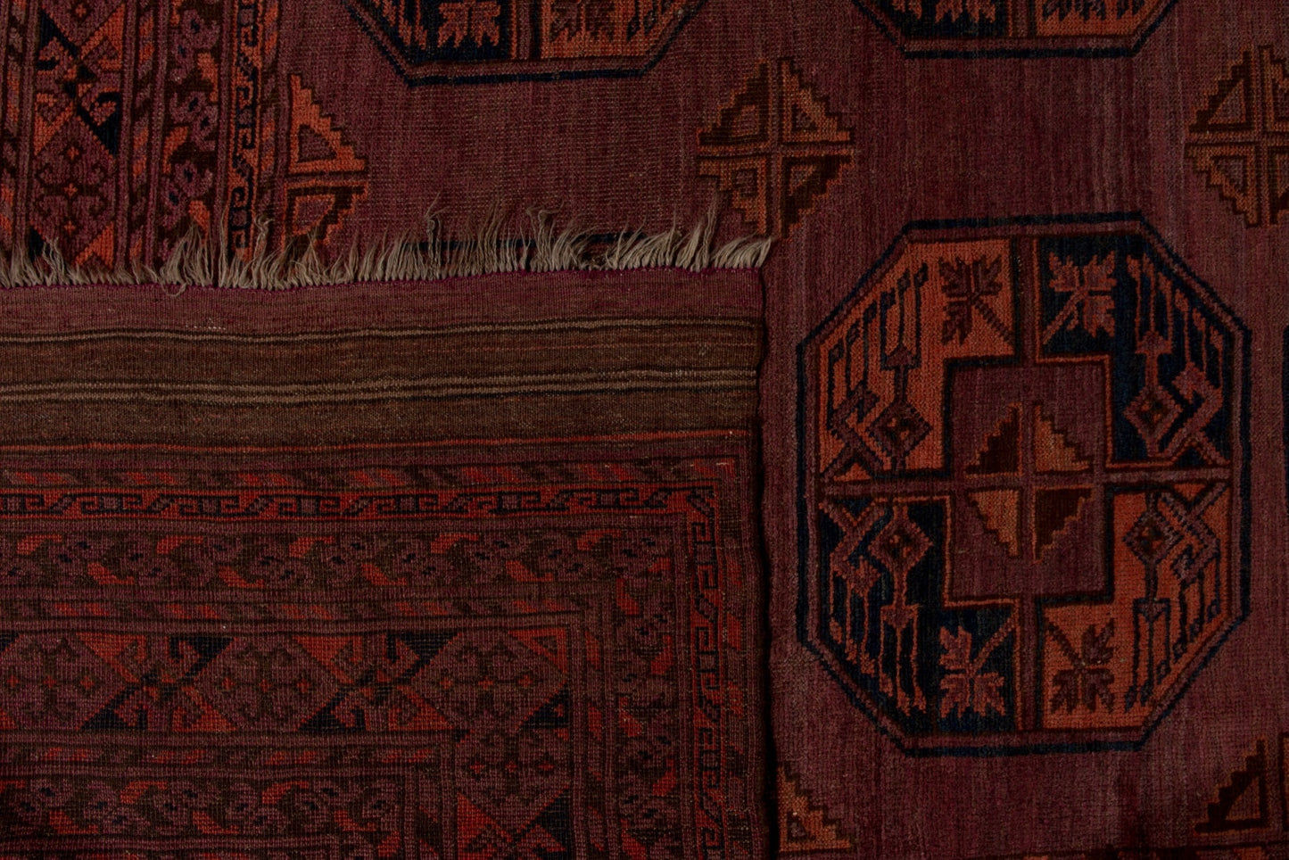 A close-up of an antique Afghan Turkmen rug featuring geometric patterns in deep red and black.