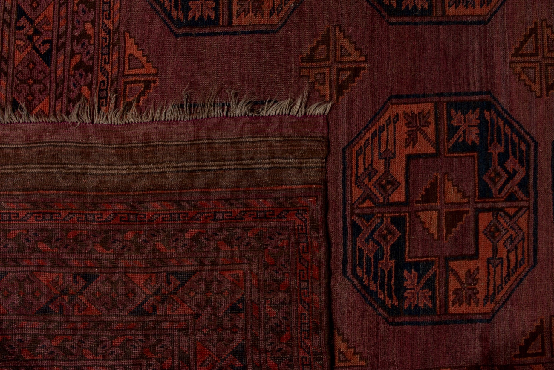 A close-up of an antique Afghan Turkmen rug featuring geometric patterns in deep red and black.