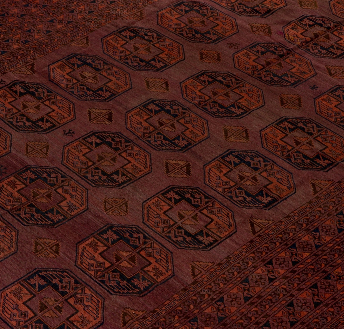 An antique Afghan Turkmen rug featuring repeating geometric octagonal motifs in red and blue wool.