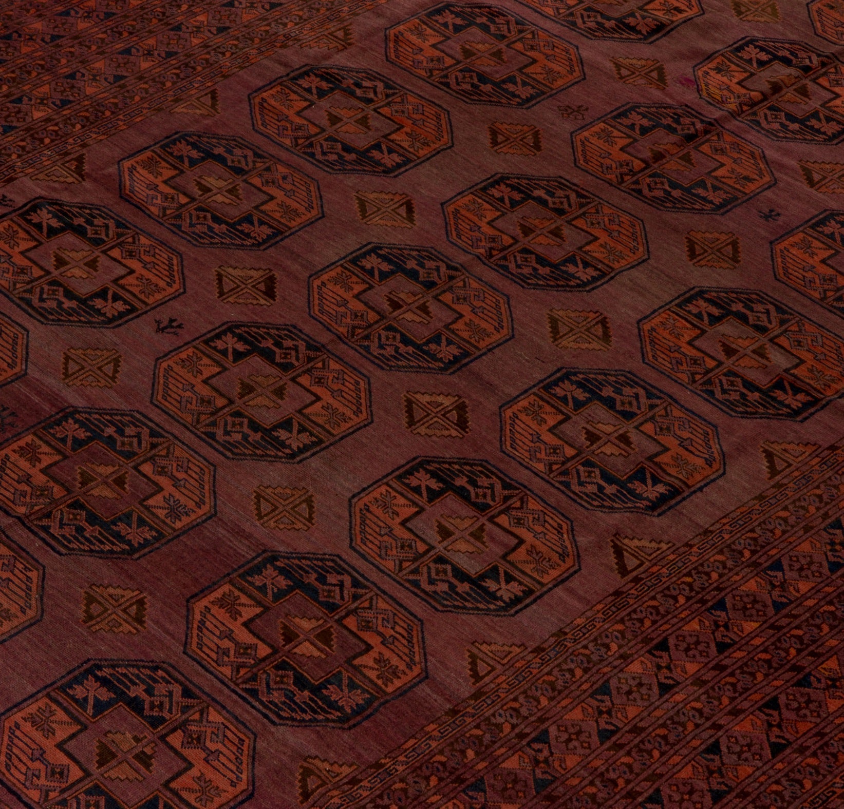 An antique Afghan Turkmen rug featuring repeating geometric octagonal motifs in red and blue wool.