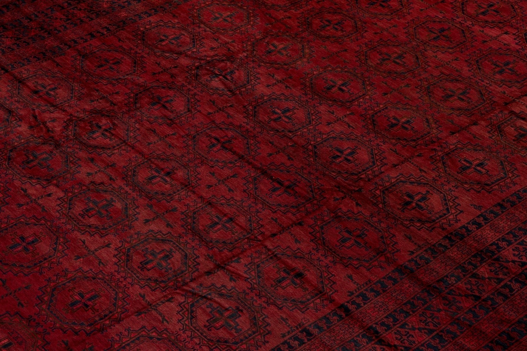 An antique Afghan Turkmen rug featuring a deep red field with repeating dark geometric motifs.